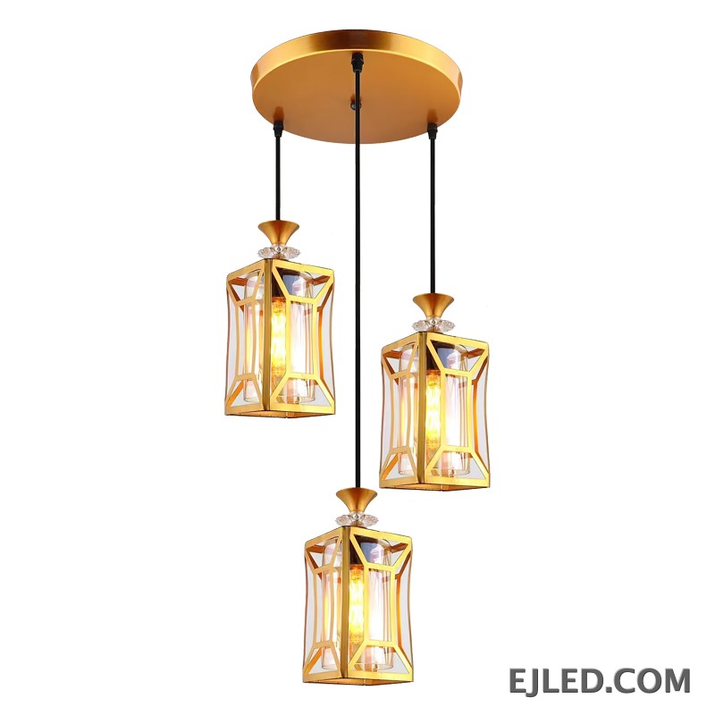 This fixture features three brass and clear glass pendant lights, each with an enclosed design, hanging from a single gold-finished canopy, casting a warm glow.