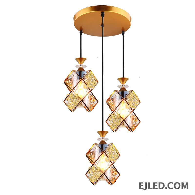This three-light pendant fixture features gold-finished frames and clear glass panels forming distinct, double-box shades. Each shade encloses a single lamp, providing warm illumination from a round gold ceiling plate.