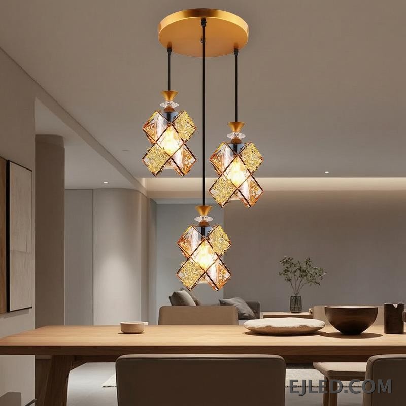 This three-light pendant fixture features gold-finished frames and clear glass panels forming distinct, double-box shades. Each shade encloses a single lamp, providing warm illumination from a round gold ceiling plate. - view 2
