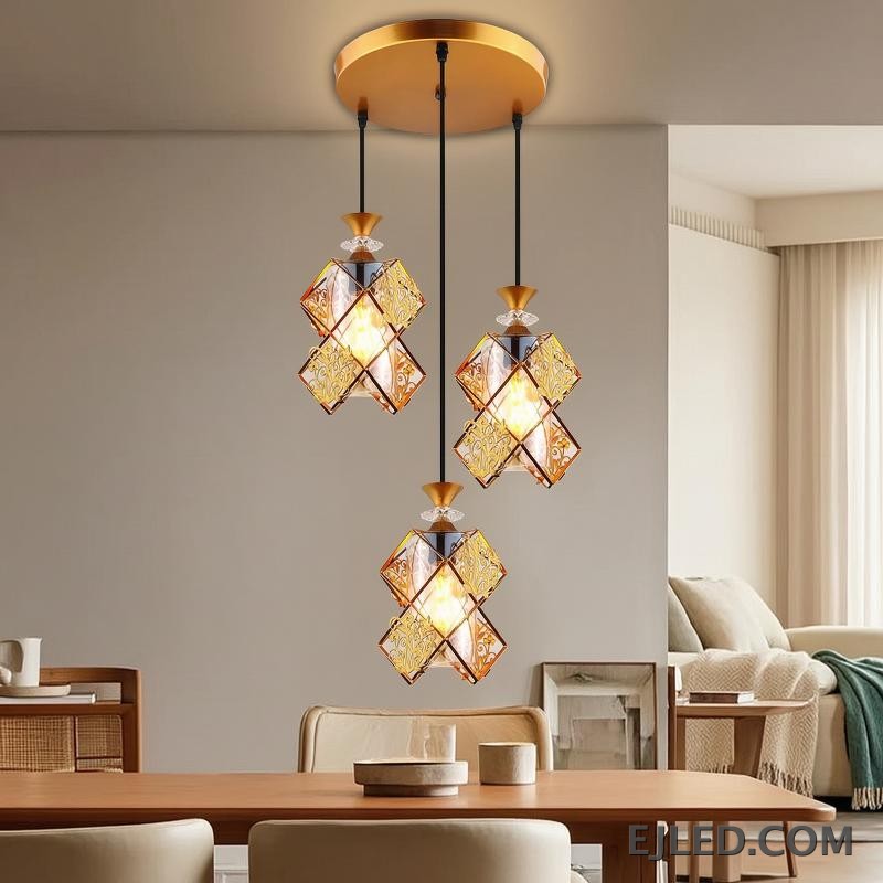 This three-light pendant fixture features gold-finished frames and clear glass panels forming distinct, double-box shades. Each shade encloses a single lamp, providing warm illumination from a round gold ceiling plate. - view 4