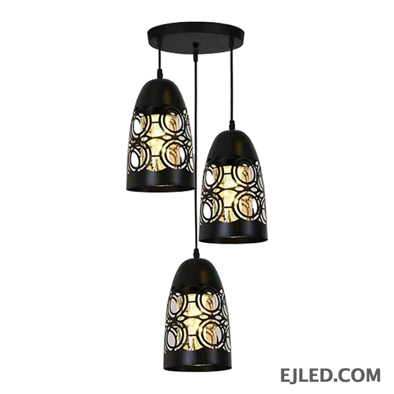 This three-light pendant cluster features black iron bell-shaped shades. Each shade has a solid top and a lower section with a distinct cut-out circular pattern, allowing light to emanate through the sides and open bottom.