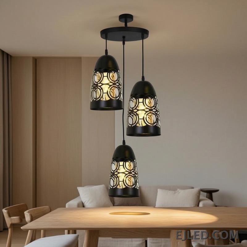This three-light pendant cluster features black iron bell-shaped shades. Each shade has a solid top and a lower section with a distinct cut-out circular pattern, allowing light to emanate through the sides and open bottom. - view 2
