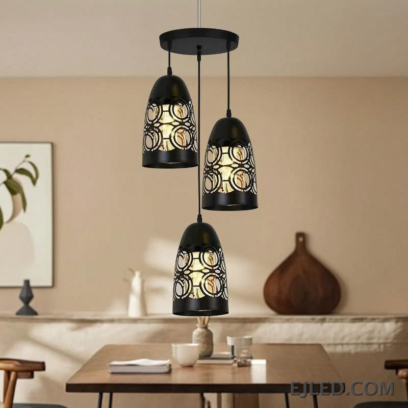 This three-light pendant cluster features black iron bell-shaped shades. Each shade has a solid top and a lower section with a distinct cut-out circular pattern, allowing light to emanate through the sides and open bottom. - view 3