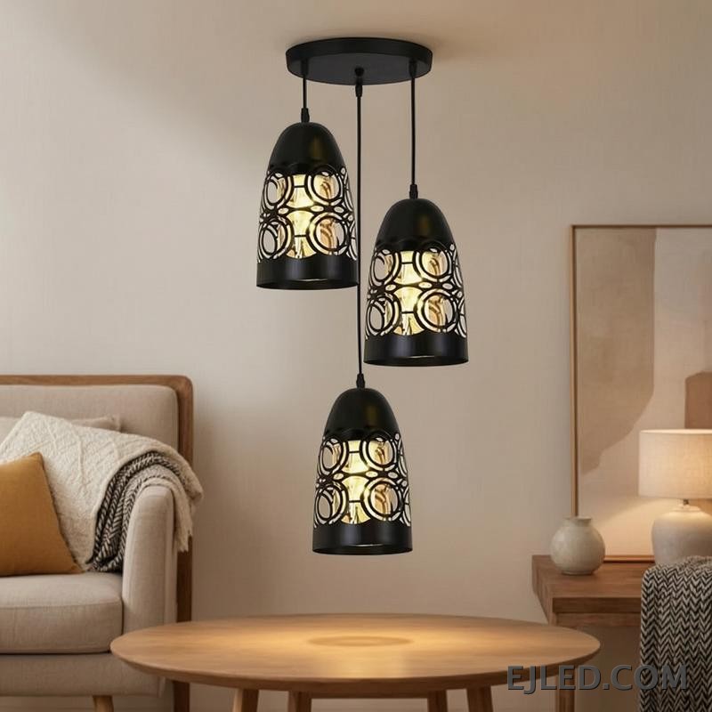 This three-light pendant cluster features black iron bell-shaped shades. Each shade has a solid top and a lower section with a distinct cut-out circular pattern, allowing light to emanate through the sides and open bottom. - view 4