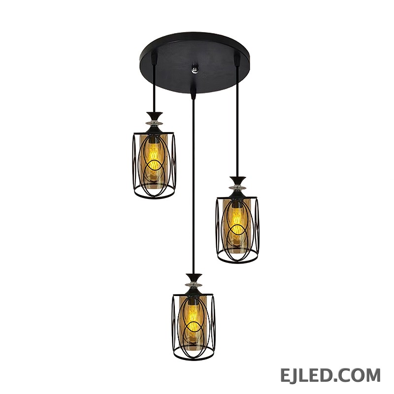 This three-lamp pendant fixture features black iron frames with cylindrical amber glass shades. Each lamp hangs from a black canopy, creating a unified lighting solution.
