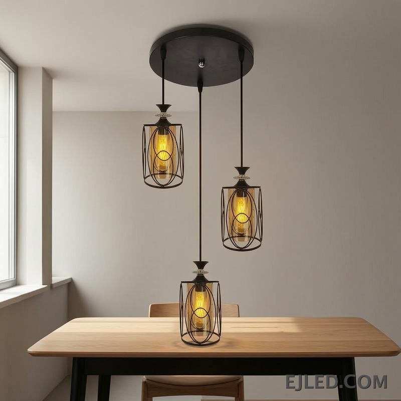 This three-lamp pendant fixture features black iron frames with cylindrical amber glass shades. Each lamp hangs from a black canopy, creating a unified lighting solution. - view 2