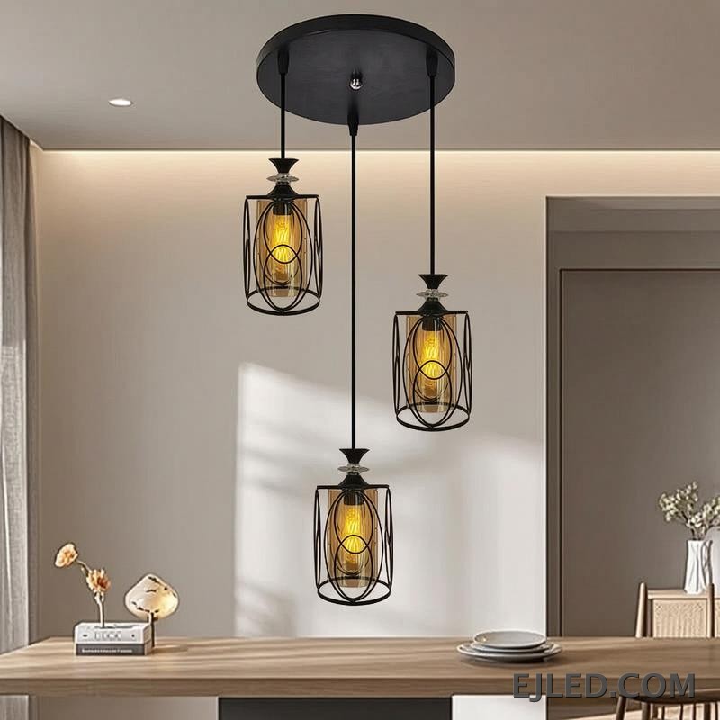 This three-lamp pendant fixture features black iron frames with cylindrical amber glass shades. Each lamp hangs from a black canopy, creating a unified lighting solution. - view 4