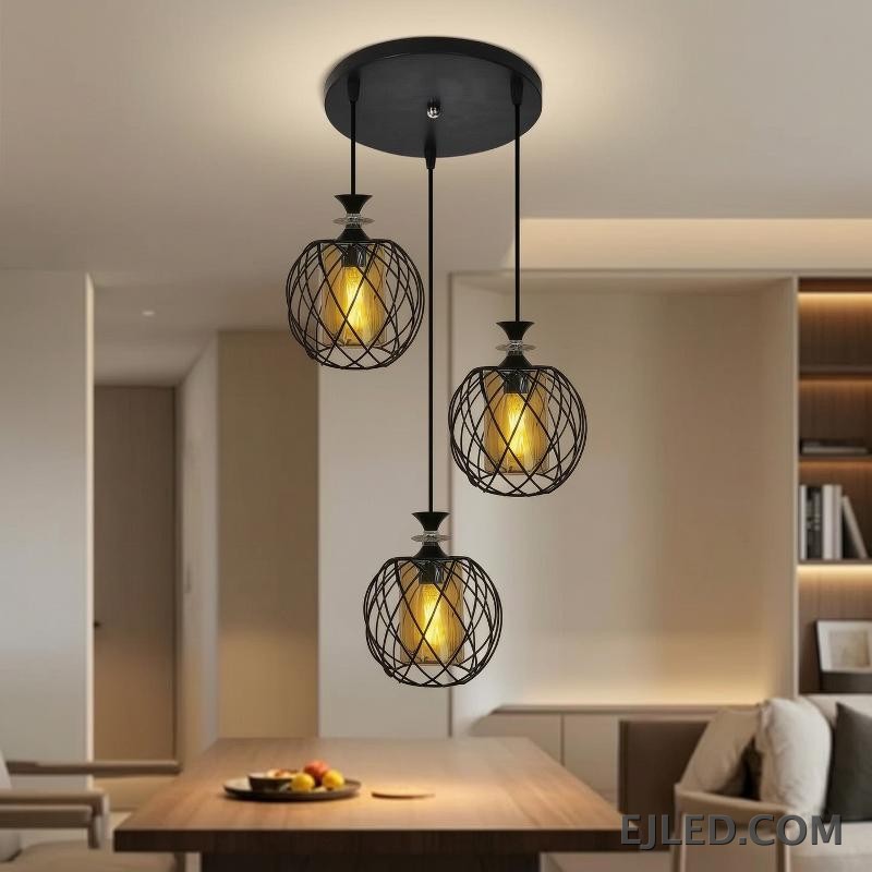 Esta lámpara colgante de múltiples luces cuenta con tres lámparas, cada una con una jaula de alambre de hierro negro que rodea un cilindro de vidrio ámbar, suspendidas de una base redonda negra de techo. - view 2