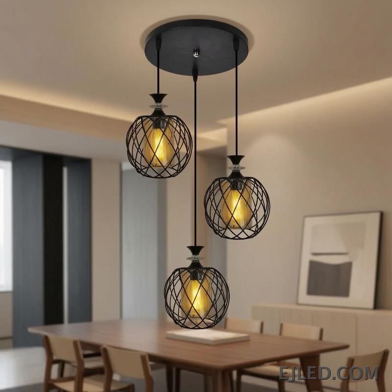 Esta lámpara colgante de múltiples luces cuenta con tres lámparas, cada una con una jaula de alambre de hierro negro que rodea un cilindro de vidrio ámbar, suspendidas de una base redonda negra de techo. - view 4