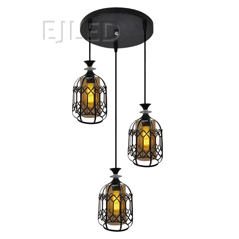This fixture features three black iron cage pendants, each with an inner amber glass shade enclosing a warm light bulb. They hang from a round black canopy, offering a distinctive industrial aesthetic.