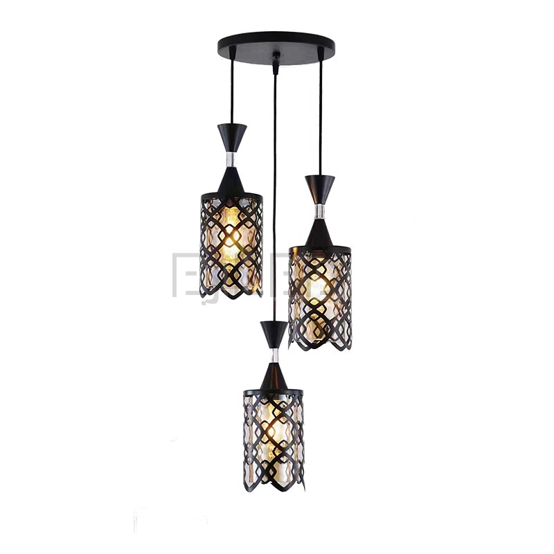 This three-light pendant features black iron cylindrical shades with an open geometric pattern over an inner amber-tinted enclosure. Each light hangs at a different length from a black circular ceiling plate, providing a warm, inviting glow.