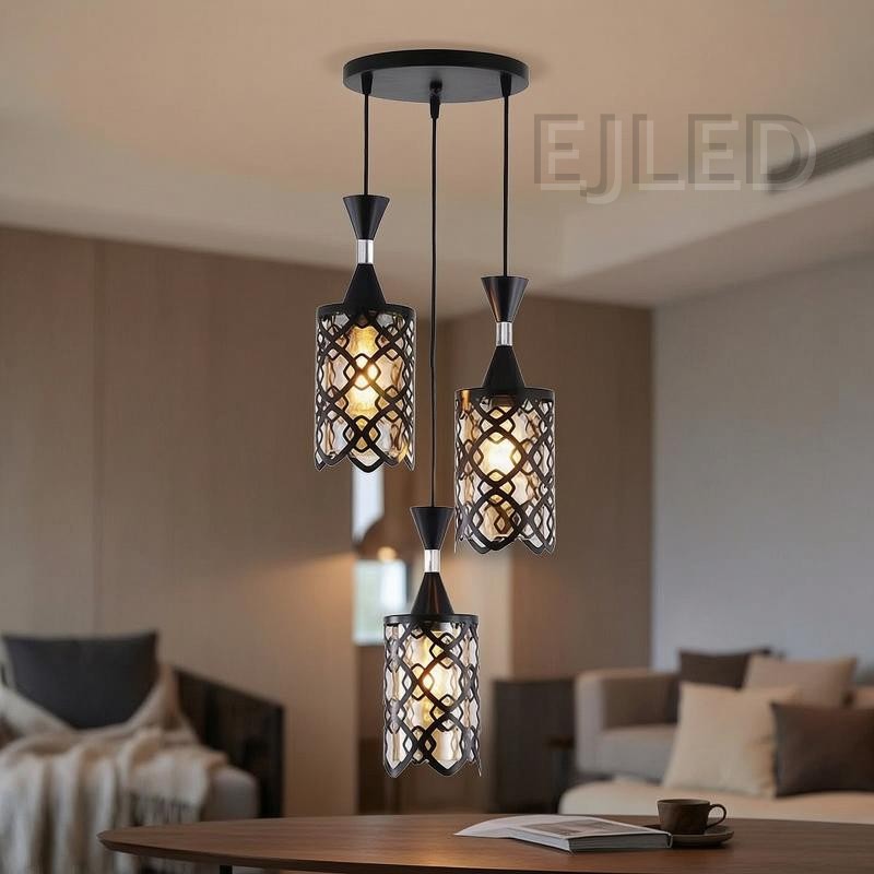 This three-light pendant features black iron cylindrical shades with an open geometric pattern over an inner amber-tinted enclosure. Each light hangs at a different length from a black circular ceiling plate, providing a warm, inviting glow. - view 2