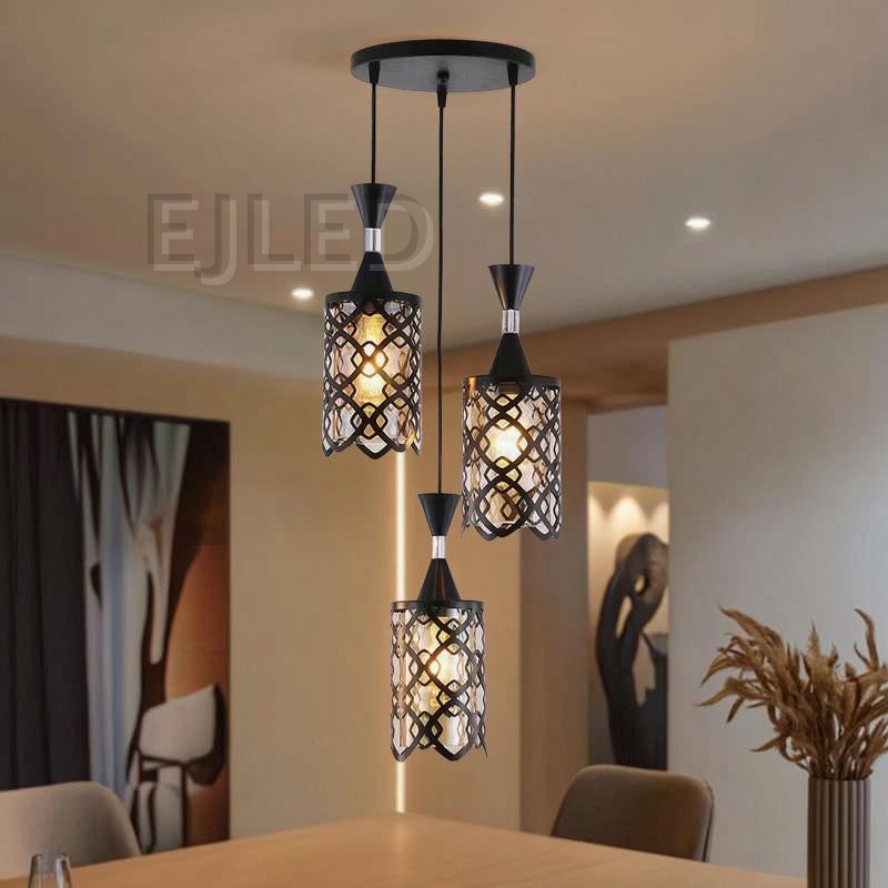 This three-light pendant features black iron cylindrical shades with an open geometric pattern over an inner amber-tinted enclosure. Each light hangs at a different length from a black circular ceiling plate, providing a warm, inviting glow. - view 3