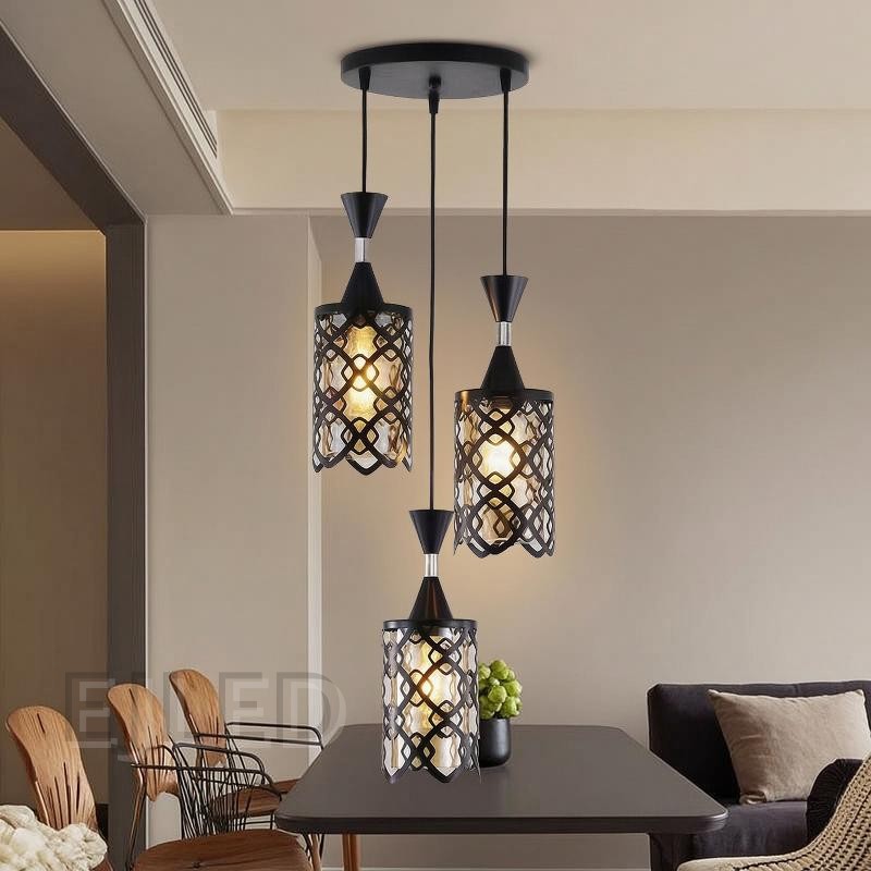 This three-light pendant features black iron cylindrical shades with an open geometric pattern over an inner amber-tinted enclosure. Each light hangs at a different length from a black circular ceiling plate, providing a warm, inviting glow. - view 4