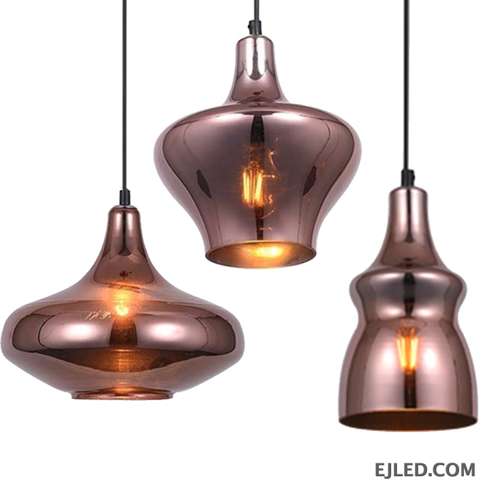 This collection features reflective copper-toned glass pendant lights in three distinct bell shapes. Each fixture houses a single bulb, providing warm, downward illumination.