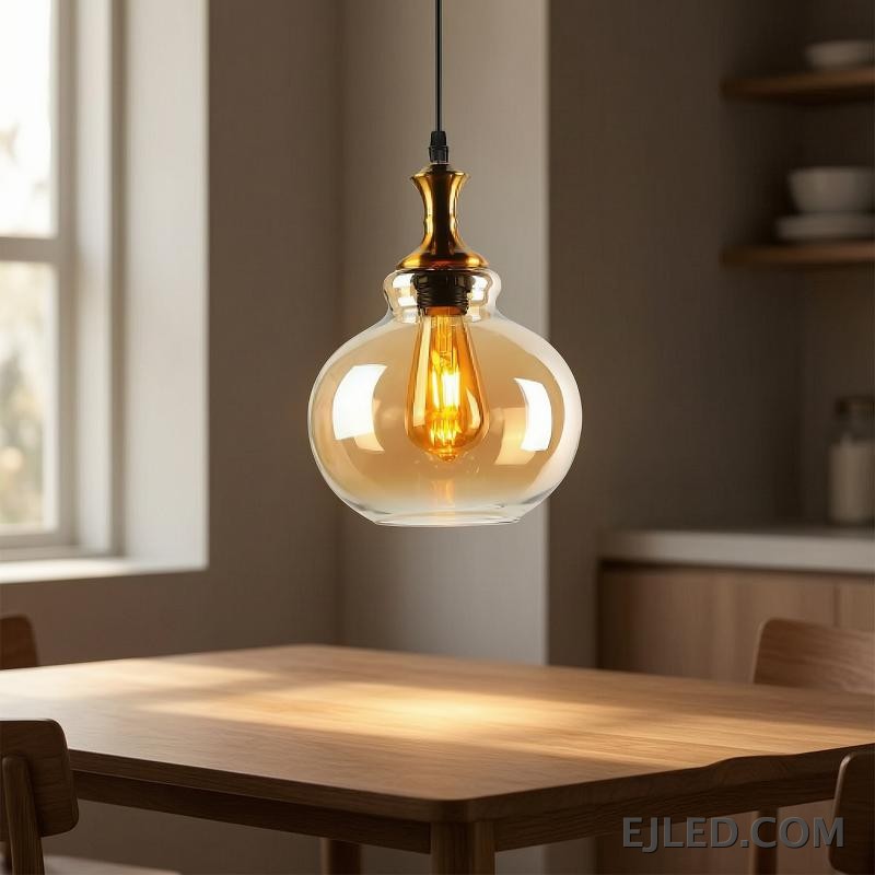 This glass pendant light features a spherical, amber-tinted shade that encloses a single exposed filament bulb. It hangs from a black suspension cord, complemented by a polished gold-finished metal cap. - view 4