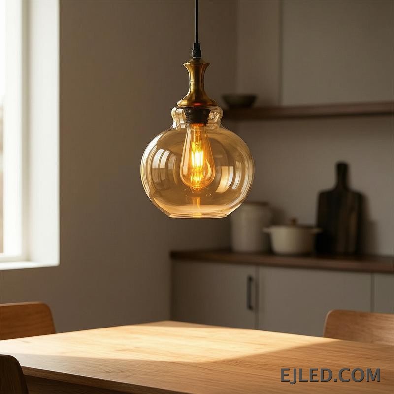 This glass pendant light features a spherical, amber-tinted shade that encloses a single exposed filament bulb. It hangs from a black suspension cord, complemented by a polished gold-finished metal cap. - view 5