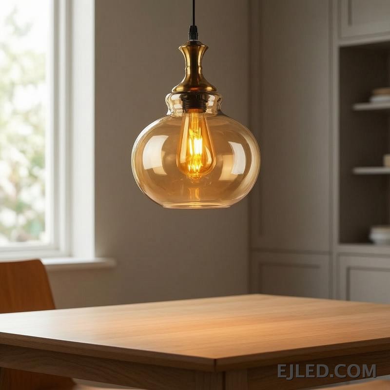 This glass pendant light features a spherical, amber-tinted shade that encloses a single exposed filament bulb. It hangs from a black suspension cord, complemented by a polished gold-finished metal cap. - view 6