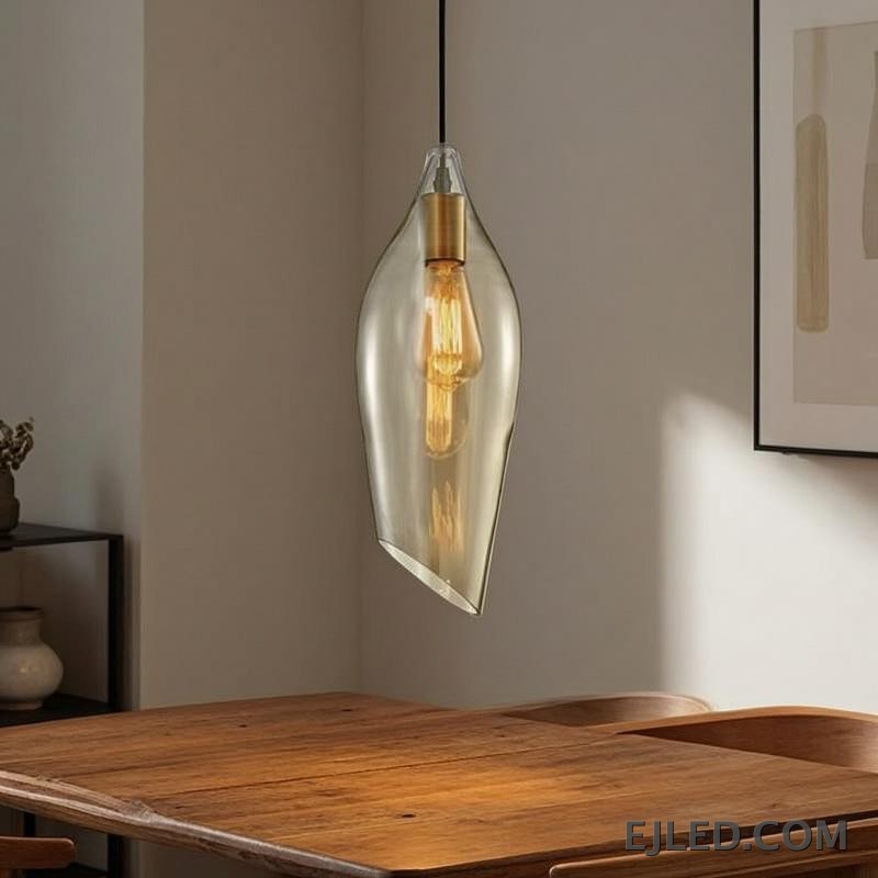 Esta lámpara colgante de cristal presenta una pantalla única asimétrica en forma de hoja con un tono ámbar cálido, que aloja una sola lámpara visible con portalámparas en tono latón. Cuelga de un cable negro sencillo y ofrece una base abierta para la difusión de la luz. - view 4