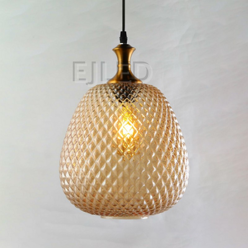 This amber textured glass pendant light features a bulbous diamond pattern shade paired with a metallic brass top and a black suspension cord. - view 2