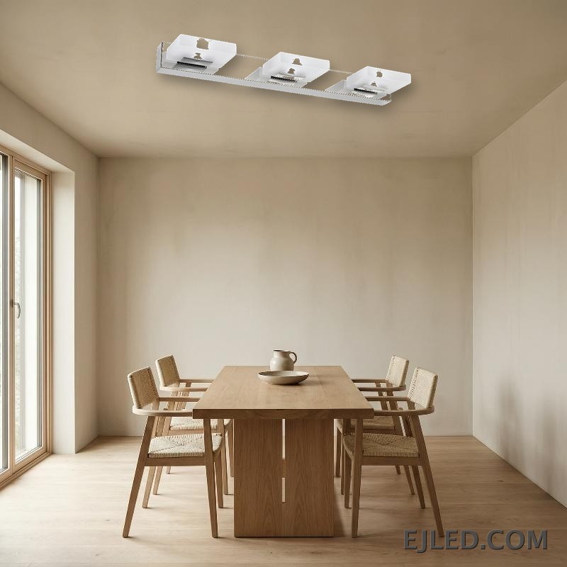 Una lámpara de espejo vertical de acero inoxidable con acabado cromado presenta tres cabezales de luz rectangulares individuales, cada uno con un difusor de acrílico blanco opaco. Su silueta limpia y vertical proporciona iluminación enfocada para áreas de trabajo en diversos entornos. - view 4