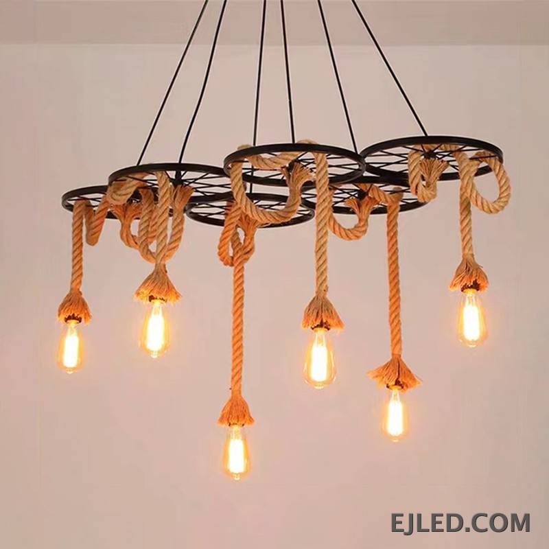 Este candelabro multiluz de cuerda de cáñamo presenta seis marcos de rueda de hierro, cada uno suspendiendo una bombilla expuesta. El diseño combina hierro robusto con elementos naturales de cuerda, creando una estética industrial para espacios comerciales. - view 5