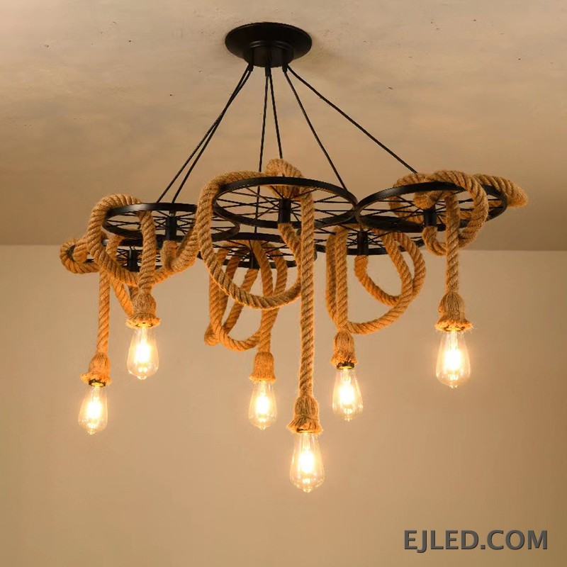 Este candelabro multiluz de cuerda de cáñamo presenta seis marcos de rueda de hierro, cada uno suspendiendo una bombilla expuesta. El diseño combina hierro robusto con elementos naturales de cuerda, creando una estética industrial para espacios comerciales. - view 6