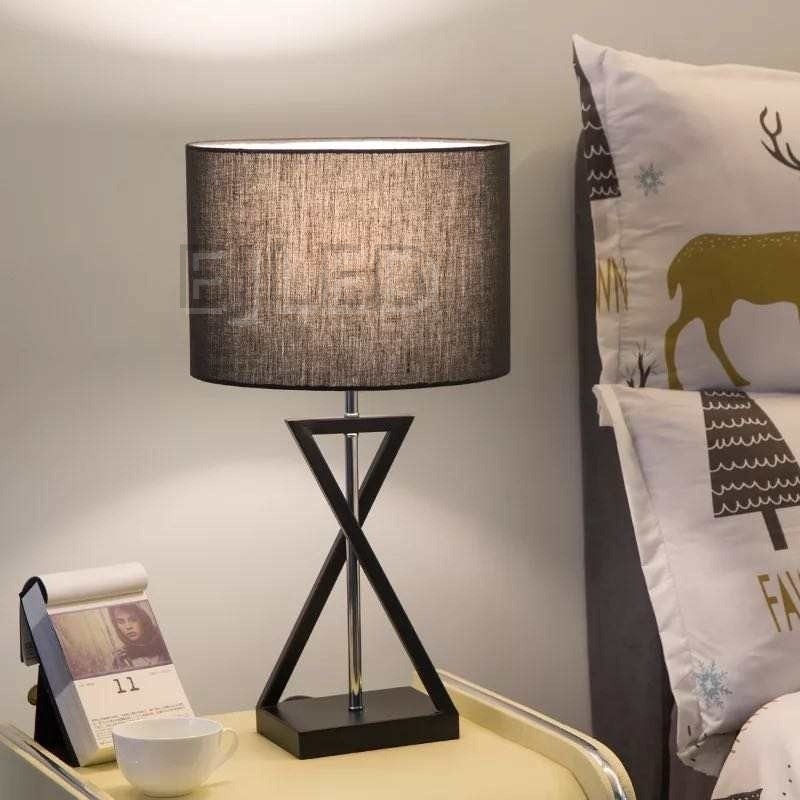 This black fabric shade table lamp features an hourglass geometric metal base in a dark finish and a central chrome support rod, blending modern lines with soft illumination for indoor spaces. - view 2