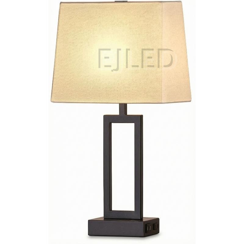 This modern table lamp features a dark metal rectangular base, an open geometric column, and a trapezoid fabric shade with built-in USB charging ports.