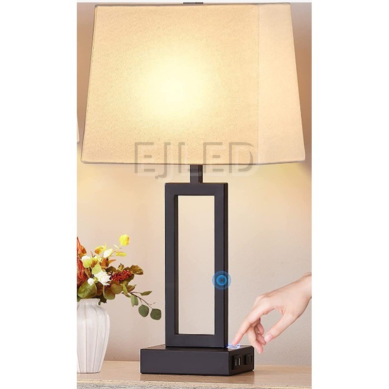 This modern table lamp features a dark metal rectangular base, an open geometric column, and a trapezoid fabric shade with built-in USB charging ports. - view 2