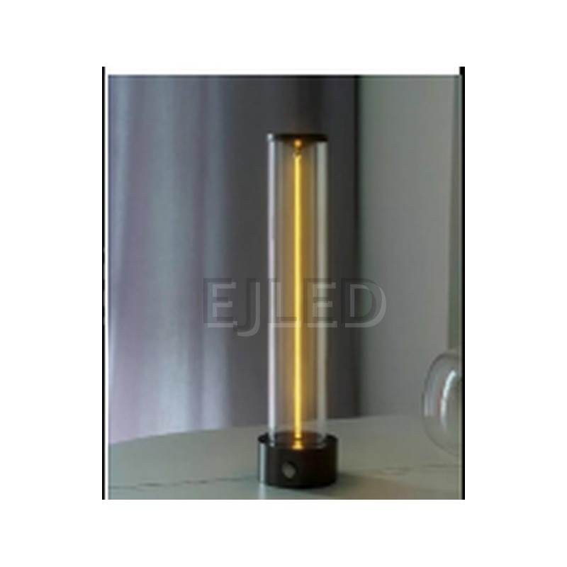 This cylindrical glass table lamp features a glowing central light tube mounted on a heavy black metal base with matching top trim. - view 2