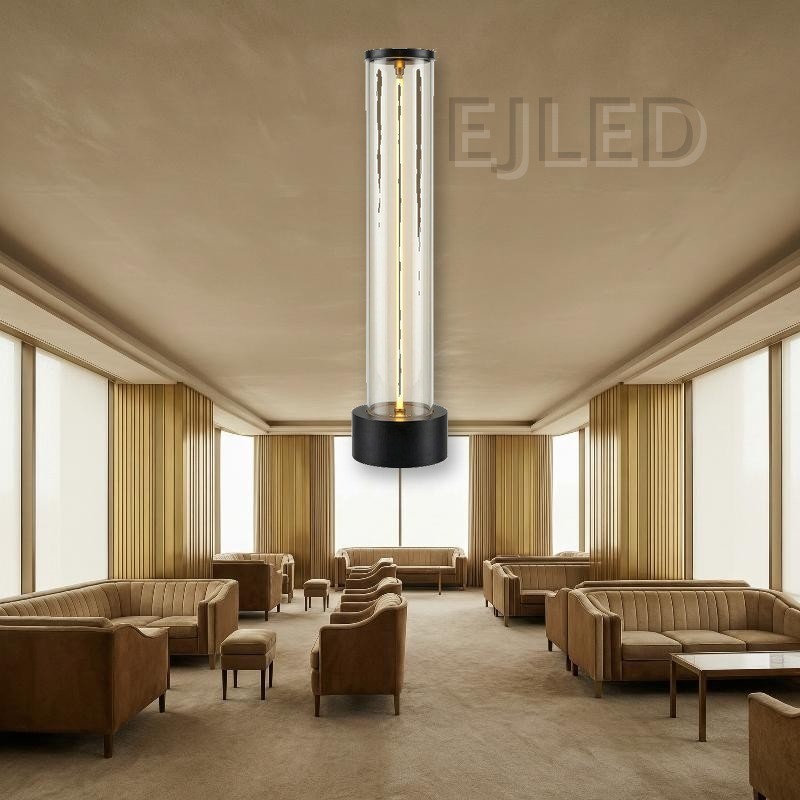 This cylindrical glass table lamp features a glowing central light tube mounted on a heavy black metal base with matching top trim. - view 4