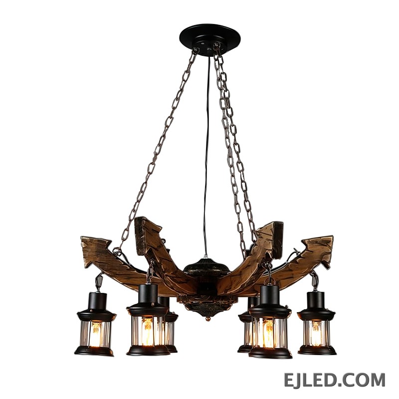 Esta lámpara colgante de madera cuenta con seis luces tipo farol suspendidas de brazos curvos de madera oscura. Cada lámpara incluye un marco de metal negro y vidrio estriado transparente, proporcionando una iluminación cálida y cerrada desde bombillas de filamento visibles.