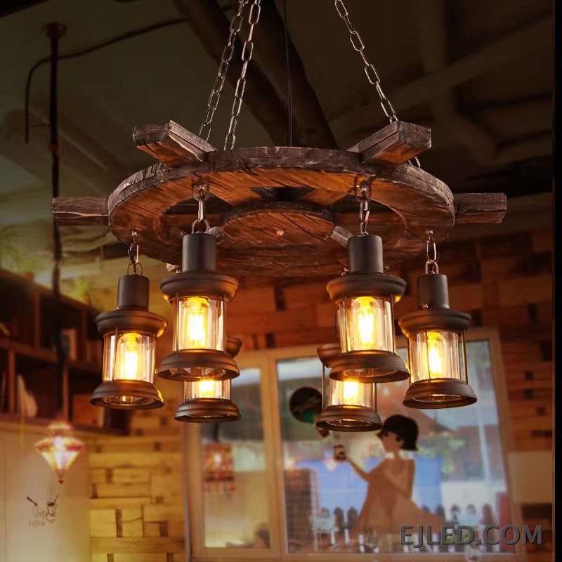 This wooden chandelier features a dark, rustic wagon wheel design with a 75cm diameter. Six clear glass lantern-style lights hang, offering an enclosed yet visible light source. - view 2