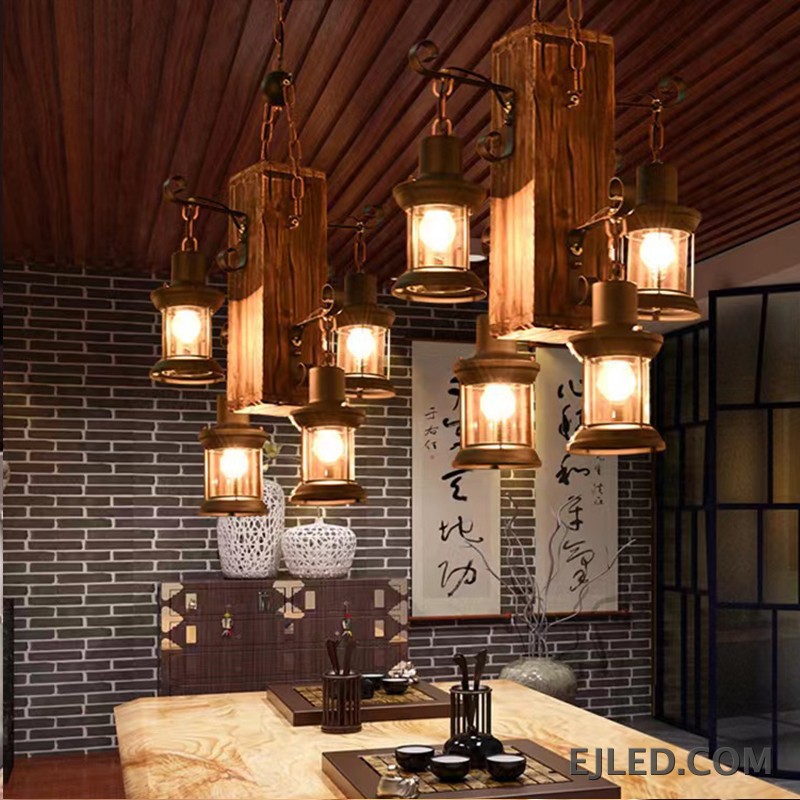 Esta lámpara colgante de madera WD0015 presenta una viga de madera envejecida que sostiene cuatro luces tipo farol. Las pantallas de vidrio transparente albergan bombillas visibles, ofreciendo un atractivo rústico para diversos proyectos de interior. - view 3