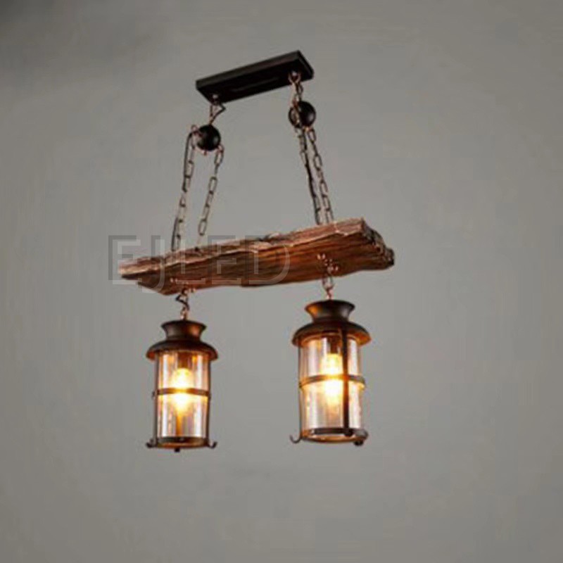 Esta lámpara presenta una viga de madera de aspecto rústico de la que cuelgan dos lámparas colgantes cilíndricas. Cada lámpara tiene una estructura de metal oscuro con paneles de vidrio transparente que emiten una luz cálida. Se cuelga mediante cadenas resistentes para un aspecto robusto. - view 2
