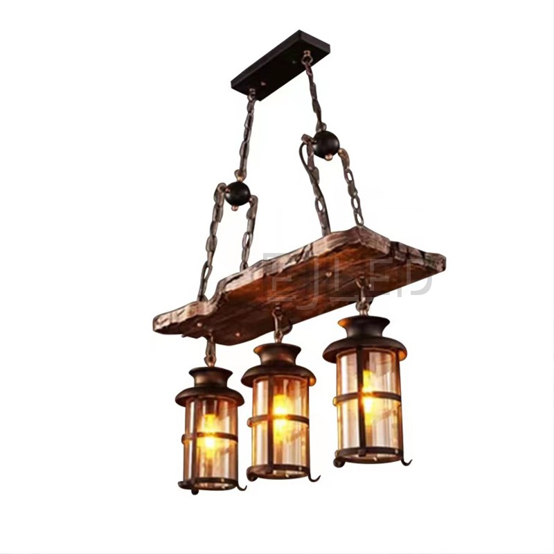 This wooden linear pendant lighting features three cylindrical lantern-style lamps suspended from a distressed wood beam. It hangs via chains from a dark metal ceiling plate, offering a rustic aesthetic.