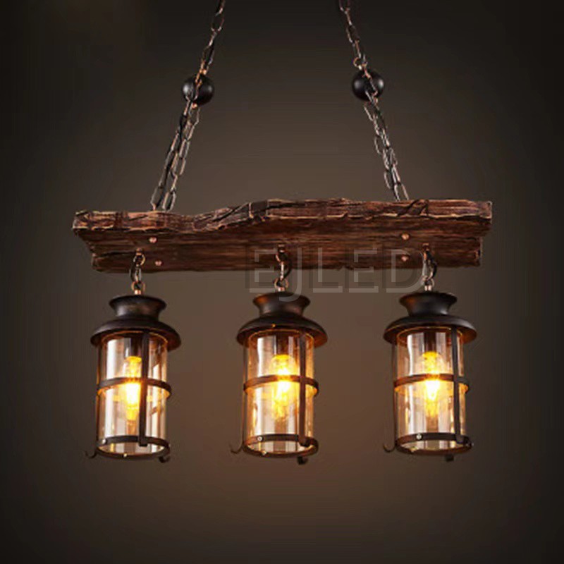 This wooden linear pendant lighting features three cylindrical lantern-style lamps suspended from a distressed wood beam. It hangs via chains from a dark metal ceiling plate, offering a rustic aesthetic. - view 2