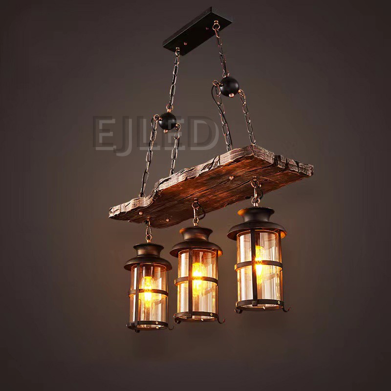 This wooden linear pendant lighting features three cylindrical lantern-style lamps suspended from a distressed wood beam. It hangs via chains from a dark metal ceiling plate, offering a rustic aesthetic. - view 4