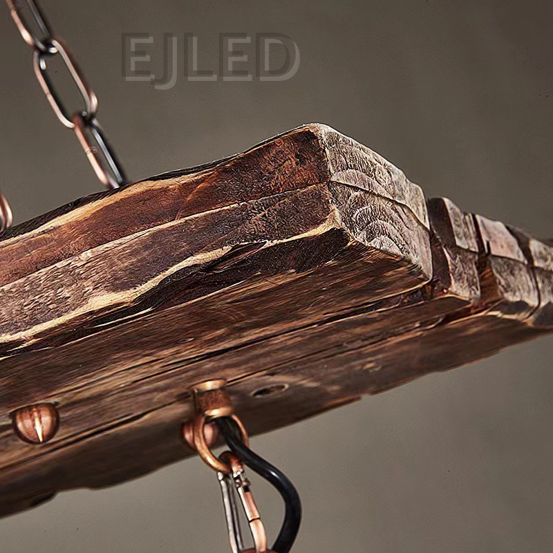 This wooden linear pendant lighting features three cylindrical lantern-style lamps suspended from a distressed wood beam. It hangs via chains from a dark metal ceiling plate, offering a rustic aesthetic. - view 6