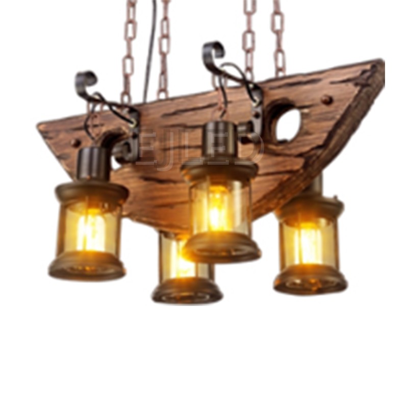 Esta lámpara colgante de madera rústica presenta una viga de madera en forma de barco suspendida por cuatro cadenas con cuatro faroles cilíndricos de vidrio y metal.
