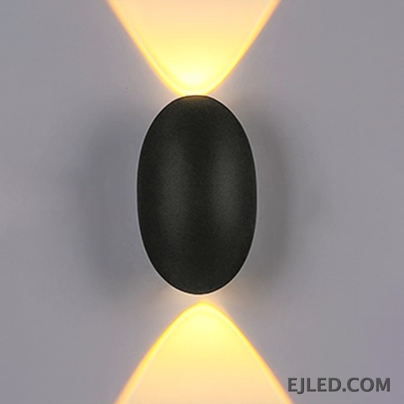 This black plastic wall light features a rounded rectangular front face and a diffused light output. It casts a soft, ambient glow upwards, downwards, and slightly forward, suitable for subtle accent illumination. - view 2