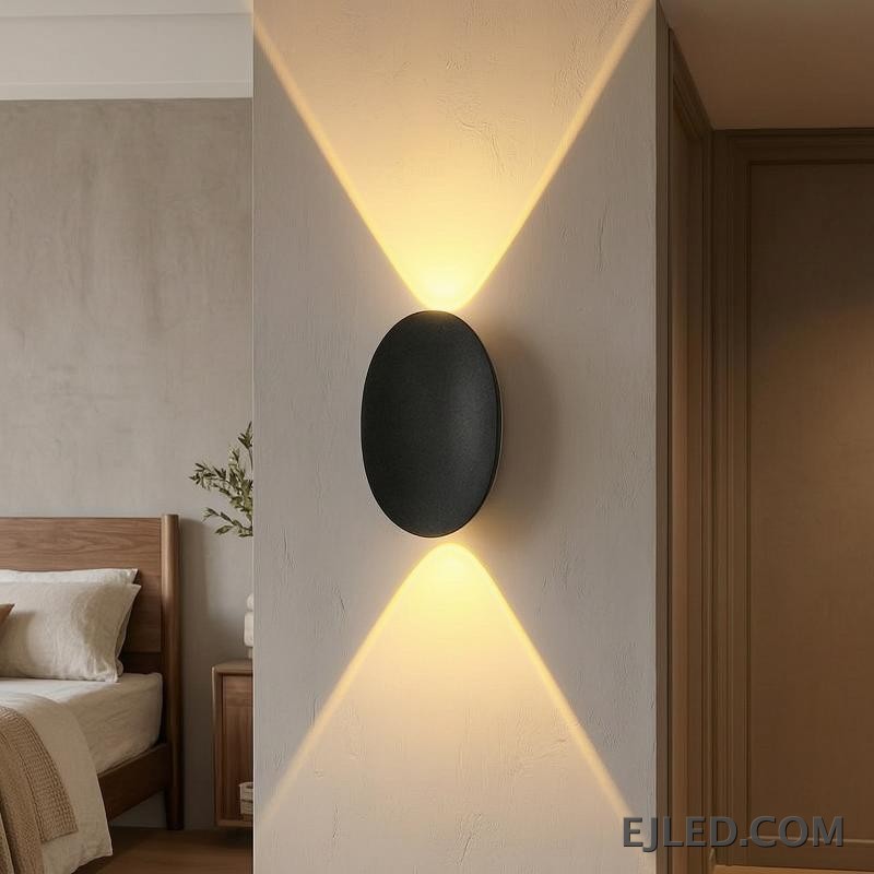 This black plastic wall light features a rounded rectangular front face and a diffused light output. It casts a soft, ambient glow upwards, downwards, and slightly forward, suitable for subtle accent illumination. - view 5