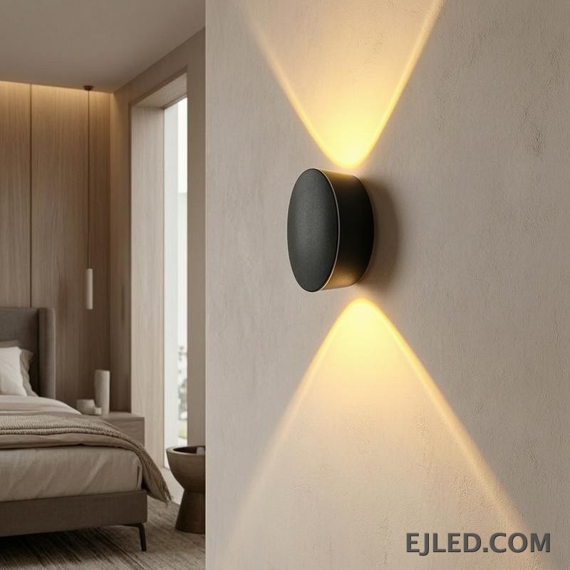 This black plastic wall light features a rounded rectangular front face and a diffused light output. It casts a soft, ambient glow upwards, downwards, and slightly forward, suitable for subtle accent illumination. - view 6