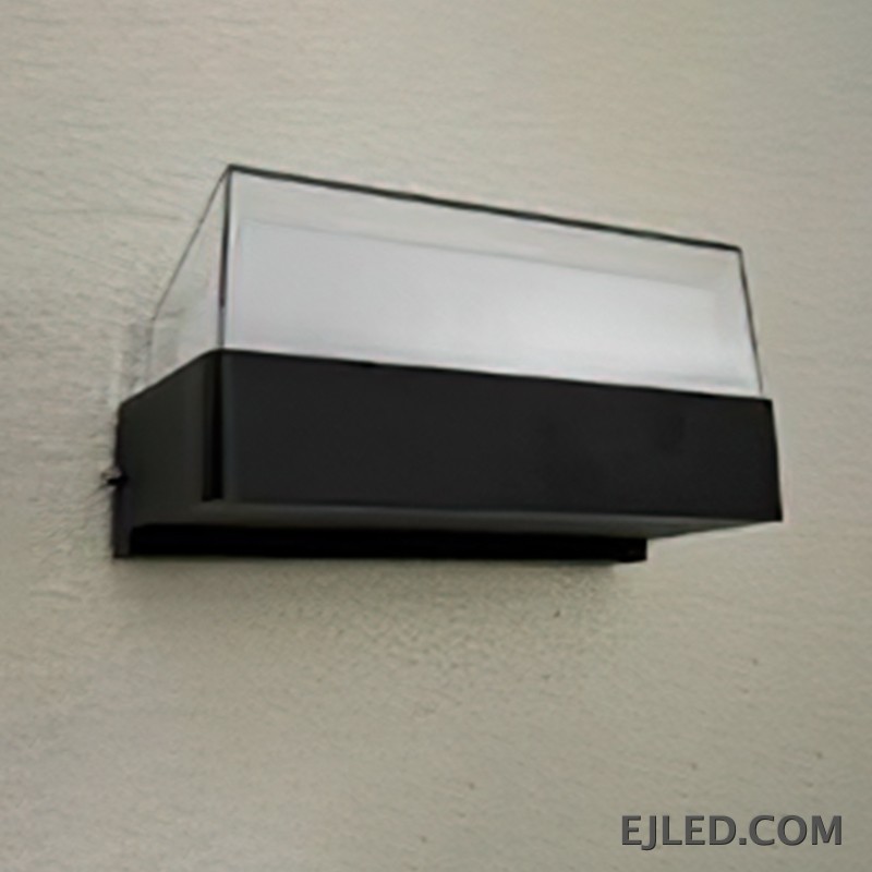 This enclosed black plastic wall light features a rectangular base and a clear sloped top diffuser, emitting soft light from its integrated source. It measures 160x85x75mm. - view 2