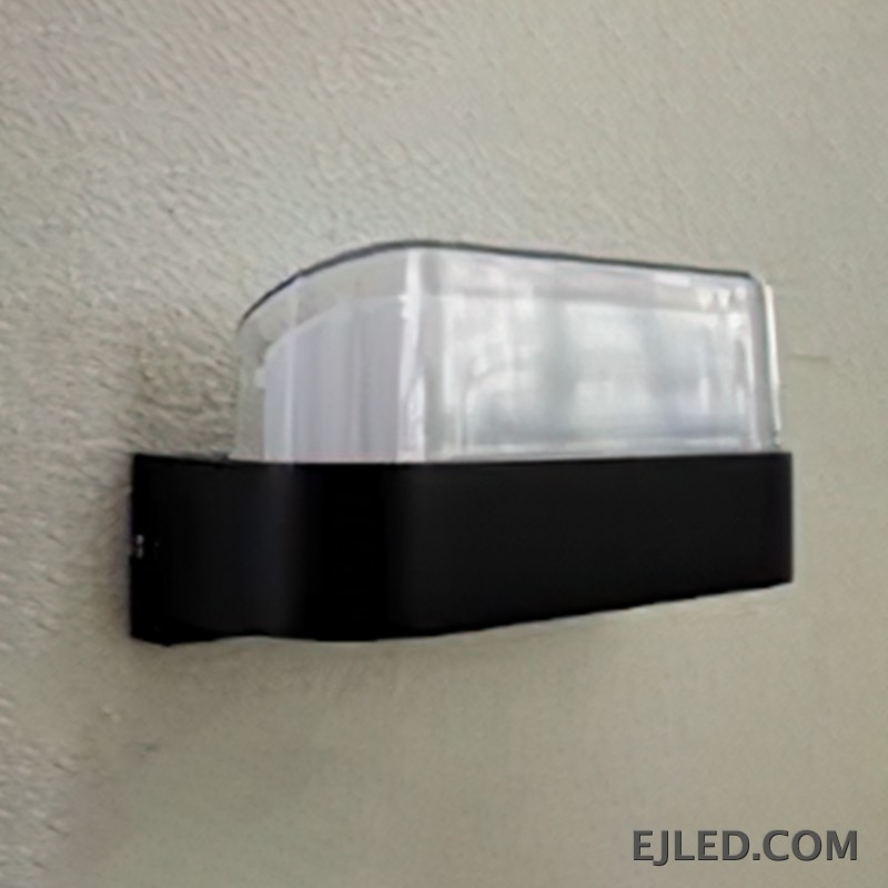 Esta lámpara de pared presenta un cuerpo rectangular de plástico con base negra y un difusor curvo de plástico transparente. Está diseñada para montaje en pared y proporciona iluminación cerrada. - view 2