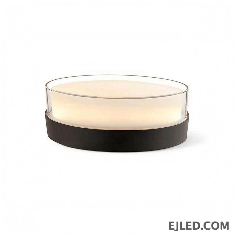 This round light fixture features a clear glass cylinder encasing a diffused white light, set upon a dark, circular base. It measures 185x80x85MM.