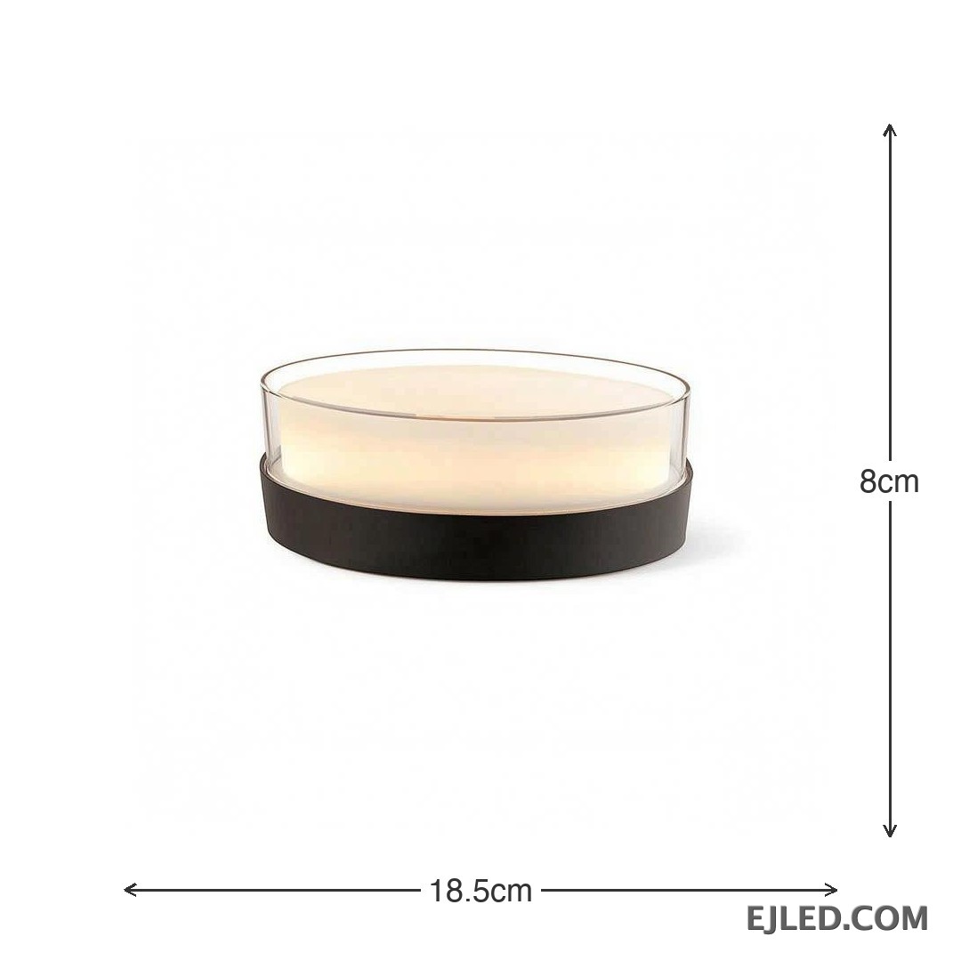This round light fixture features a clear glass cylinder encasing a diffused white light, set upon a dark, circular base. It measures 185x80x85MM. - view 3
