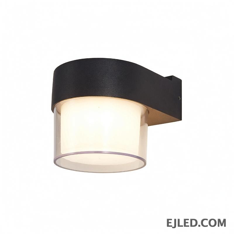This wall lamp features a textured black plastic body with a curved arm, enclosing a cylindrical light source. It has an inner frosted diffuser and an outer clear enclosure for emitted light.