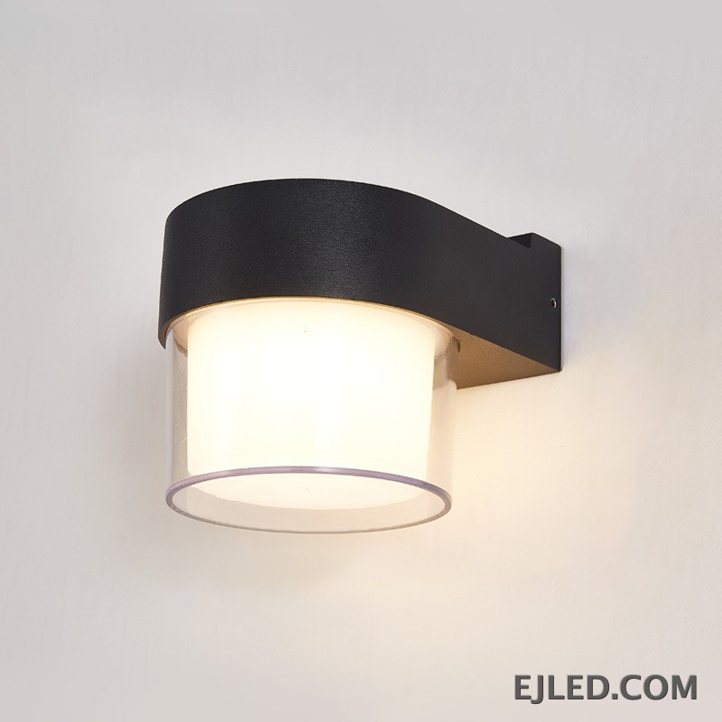 This wall lamp features a textured black plastic body with a curved arm, enclosing a cylindrical light source. It has an inner frosted diffuser and an outer clear enclosure for emitted light. - view 2